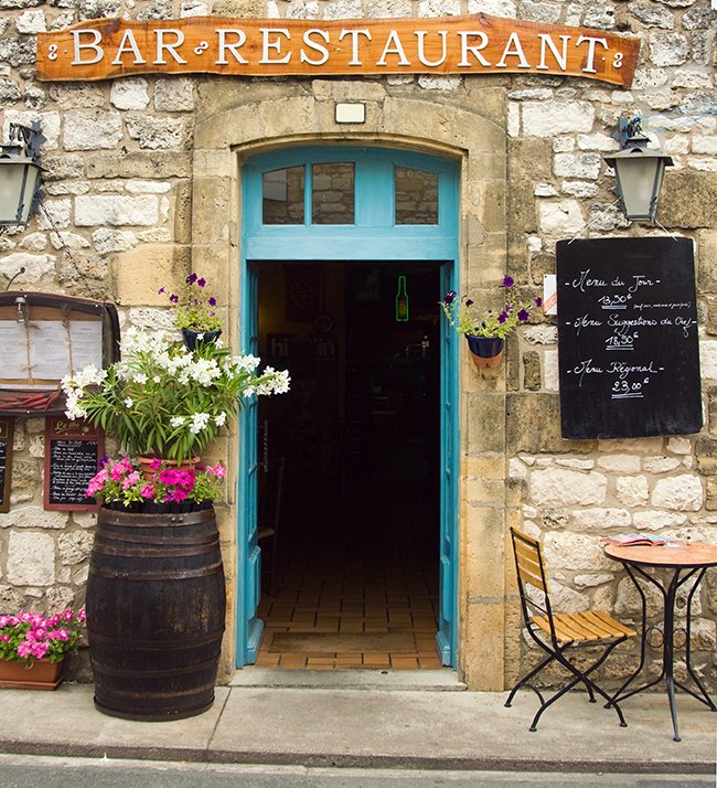 old stone restaurant and bar exterior entrance with wooden barrel and flowers